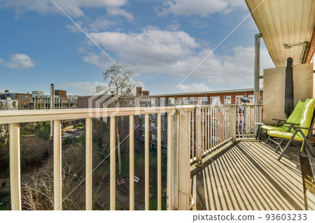 Narrow brick balcony with metal railings, wooden chair and door 93603233