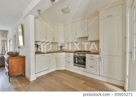 Modern minimalist style interior design of studio apartment with open white kitchen and dining zone with table and chairs illuminated by loft style lamp Modern minimalist style interior design of studio apartment with open white kitchen and dining zone with table and chairs illuminated by loft style lamp 93603271