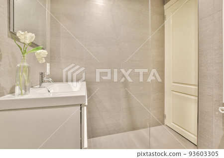 Cupboard with sink and mirror attached to tiled wall near door and drying rack in modern restroom 93603305