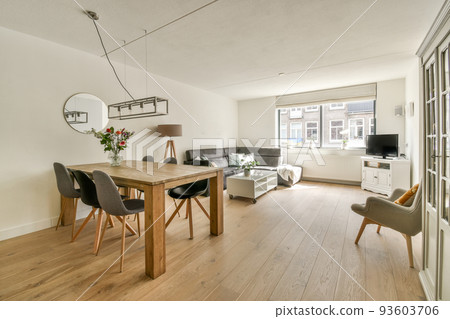 Contemporary minimalist style interior design of light studio apartment with wooden table and chairs in dining zone between open kitchen and living room with white walls and parquet floor 93603706