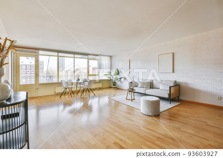 Stylish interior design of living room with light furniture and soft comfy couch and carpet in modern apartment with open kitchen and white walls 93603927