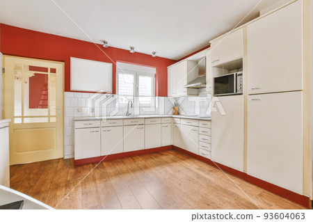 Fragment of interior of light narrow home kitchen with minimalist style white furniture with sink and stove 93604063