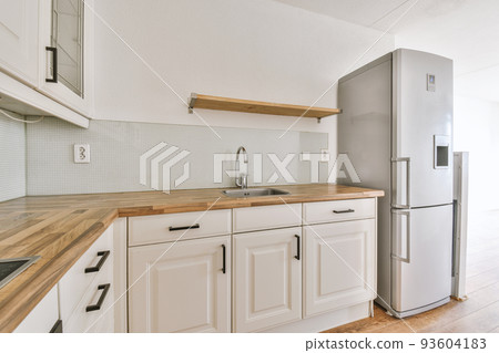 Fragment of interior of light narrow home kitchen with minimalist style white furniture with sink and stove Fragment of interior of light narrow home kitchen with minimalist style white furniture with sink and stove 93604183