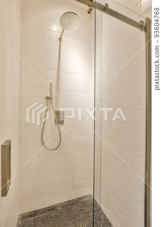 Shower faucets attached to tiled wall near glass partition and ornamental curtail in washroom at home 93604768