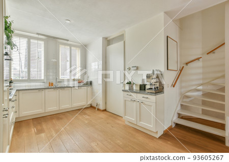 Modern minimalist style interior design of studio apartment with open white kitchen and dining zone with table and chairs illuminated by loft style lamp 93605267