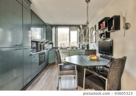 Modern minimalist style interior design of studio apartment with open white kitchen and dining zone with table and chairs illuminated by loft style lamp 93605323