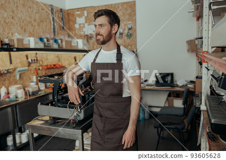 Repairman in uniform standing on workshop of coffee machines warehouse and looking awat Repairman in uniform standing on workshop of coffee machines warehouse and looking awat 93605628