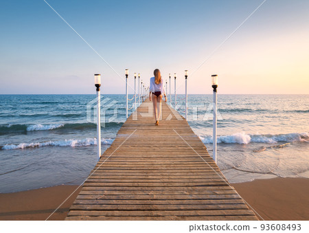 Happy young woman in bikini walking on wooden pier on the sea Happy young woman in bikini walking on wooden pier on the sea 93608493