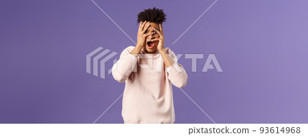Portrait of shocked, startled handsome man being embarrassed and scared of seeing something unappropriate and awkward, cover eyes but peeking through fingers from interest Portrait of shocked, startled handsome man being embarrassed and scared of seeing something unappropriate and awkward, cover eyes but peeking through fingers from interest 93614968
