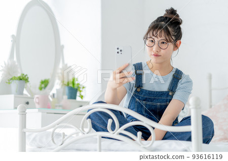 High school girl sitting cross-legged on the bed and operating a smartphone 93616119