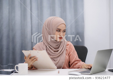Happy asian muslim woman brown hijab working at home with laptop and documents. 93621477