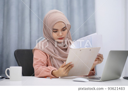 Happy asian muslim woman brown hijab working at home with laptop and documents. Happy asian muslim woman brown hijab working at home with laptop and documents. 93621483