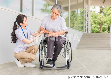An elderly person on a wheelchair holding a caregiver and a stomach An elderly person on a wheelchair holding a caregiver and a stomach 93624924
