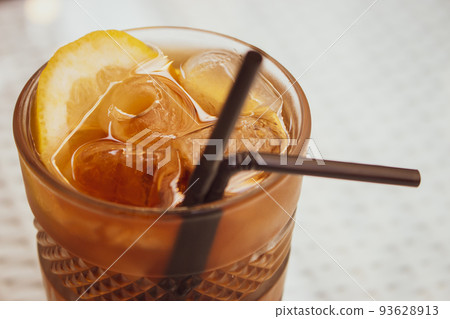 Long Island cocktail with drinking straw. Alcoholic cocktail with ice cubes and lemon slice. Cold drinks. Party background. Bar table with cocktail.  93628913