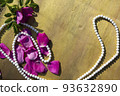 Pink rose petals and beads on a wooden background. 93632890