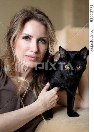 young woman posing with cute black cat with yellow eyes in her hands close up portrait 93633771