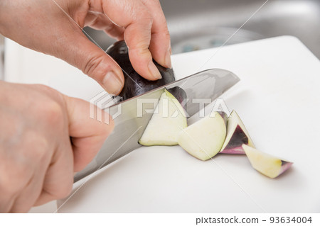 [A middle-aged housewife cuts an eggplant into chunks with a Santoku knife] 93634004