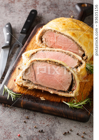 High angle beef wellington cooking or boeuf en crout cut into slices on a chopping board. Vertical High angle beef wellington cooking or boeuf en crout cut into slices on a chopping board. Vertical 93635156