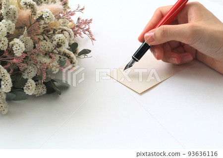 一張留言卡、一支紅筆和一朵天然乾花一個女人的手拿著筆，試圖在卡片上寫字 93636116
