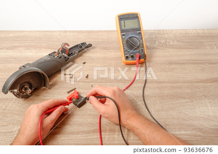 Power tool repair. A man repairs an angle grinder. Screwdriver, multimeter. Details of electrical appliance 93636676
