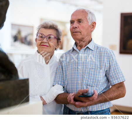 mature European couple examines paintings in an exhibition in hall of art museum 93637622