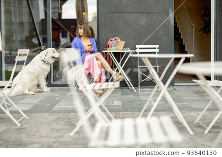 Woman sits with her adorable white dog at cafe on a street 93640130