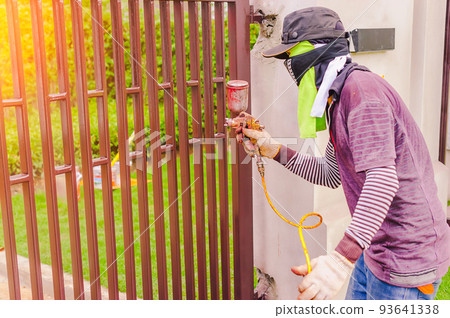 Male workers are using a paint sprayer at a steel door. Workers spray paint must be protected from inhalation by using cloth to cover the nose. Male workers are using a paint sprayer at a steel door. Workers spray paint must be protected from inhalation by using cloth to cover the nose. 93641338
