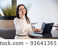 Smiling woman working on laptop and smartphone 93641365