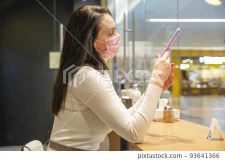 woman in medical mask in public place. portrait of woman in cafe typing smartphone woman in medical mask in public place. portrait of woman in cafe typing smartphone 93641366