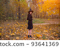 woman in witch costume with broom walking on covered with falling autumn leaves Halloween day forest 93641369