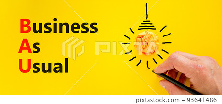 BAU business as usual symbol. Concept words BAU business as usual on a beautiful yellow background. Orange light bulb icon. Businessman hand. Business and BAU business as usual concept. Copy space. BAU business as usual symbol. Concept words BAU business as usual on a beautiful yellow background. Orange light bulb icon. Businessman hand. Business and BAU business as usual concept. Copy space. 93641486