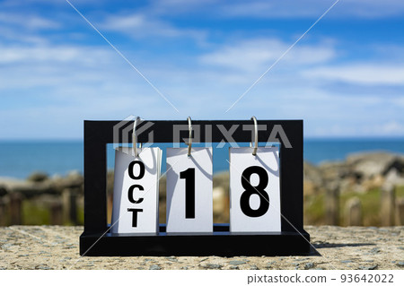 Oct 18 calendar date text on wooden frame with blurred background of ocean. 93642022
