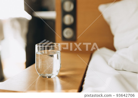 Glass of water on wooden table bokeh background. Good habit - drinking a glass of water before going to sleep. Modern and comfortable home or hotel bedroom interior 93642706