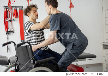 Rehabilitation specialist helps man to get up from a wheelchair at clinic Rehabilitation specialist helps man to get up from a wheelchair at clinic 93643020