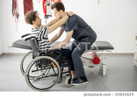 Rehabilitation specialist helps man to get up from a wheelchair at clinic Rehabilitation specialist helps man to get up from a wheelchair at clinic 93643024