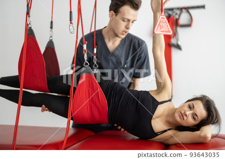 Rehabilitation specialist doing active treatment on suspension straps to a male patient 93643035