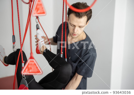 Rehabilitation specialist doing active treatment on suspension straps to a male patient 93643036