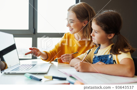 Cheerful mother doing homework with daughter at home 93643537