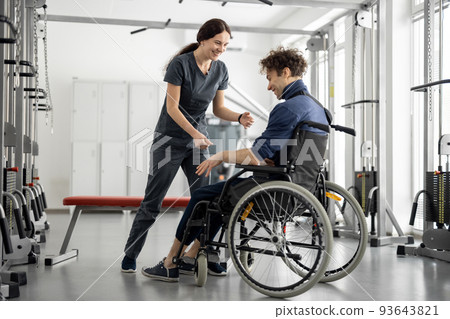 Rehabilitation specialist helps a guy stand out of a wheelchair 93643821