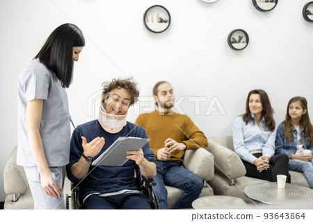 Medical worker communicates with guy in wheelchair at the clinic reception 93643864