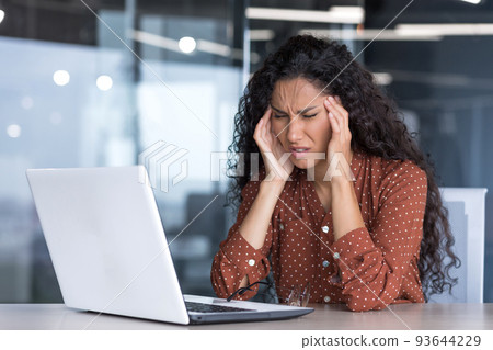 Sick and overtired Latin American business woman working inside office building, female worker holding her head with hands having severe headache and migraine Sick and overtired Latin American business woman working inside office building, female worker holding her head with hands having severe headache and migraine 93644229