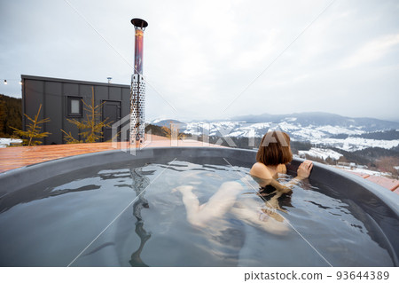 Woman swims in hot bath while resting at small modern house in the mountains 93644389