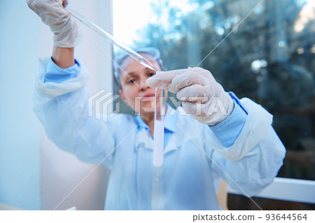Selective focus. Test tube with a chemical substance in the hands of a chemist, using a graduated pipette and titrating a reagent in a medical science laboratory, while conducting a clinical study Selective focus. Test tube with a chemical substance in the hands of a chemist, using a graduated pipette and titrating a reagent in a medical science laboratory, while conducting a clinical study 93644564