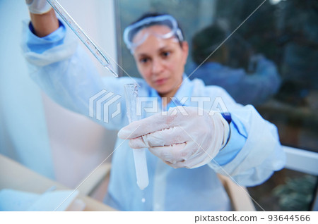 Selective focus on a test tube with a taking place chemical reaction and graduated lab pipette in a blurred woman scientist hands dripping reagent, conducting science experiment in research laboratory 93644566
