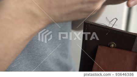 Man working with leather by needle. Genuine Leather. Sewing a purse. Leather work. Tools for sewing bags, wallets, clutches. Stitching. Manual sewing of the product. 93646386