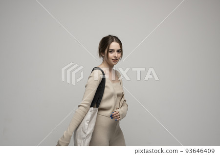 Beautiful brunette woman in a beige costume with cotton bag on a shoulder on a grey background. Mockup and zero waste concept. Beautiful brunette woman in a beige costume with cotton bag on a shoulder on a grey background. Mockup and zero waste concept. 93646409
