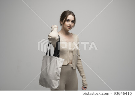 Beautiful brunette woman in a beige costume with cotton bag on a shoulder on a grey background. Mockup and zero waste concept. 93646410
