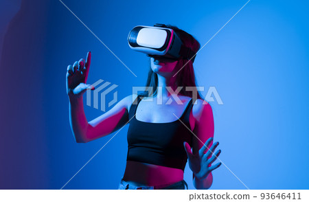 Virtual reality concept. Young brunette woman wearing a VR headset and looking up while playing a game with a friends in a metaverse. Virtual reality concept. Young brunette woman wearing a VR headset and looking up while playing a game with a friends in a metaverse. 93646411
