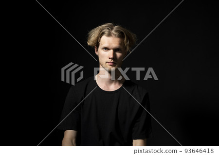 Portrait of calm serious mature young man without emotions. Beautiful emotionless guy in a black t-shirt looking to the camera, isolated over black background. Portrait of calm serious mature young man without emotions. Beautiful emotionless guy in a black t-shirt looking to the camera, isolated over black background. 93646418