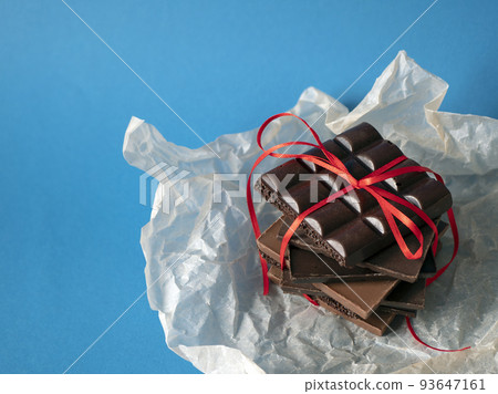 Chocolate pieces with a red ribbon on the blue background. Concept of surprise, sweet gift, love and romance Chocolate pieces with a red ribbon on the blue background. Concept of surprise, sweet gift, love and romance 93647161